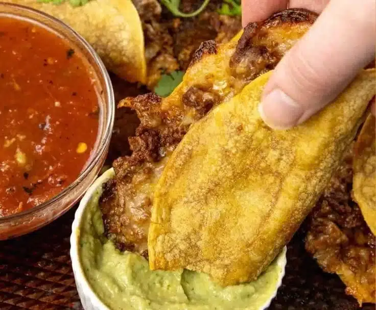 Plate of crispy beef tacos topped with fresh ingredients and salsa.